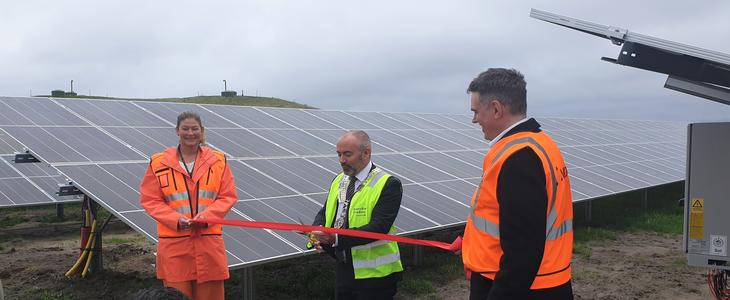 Lufthavndirektør, ordfører og statsekretær i oransje og gult synglighetstøy foran nytt stort solcelleanlegg. 