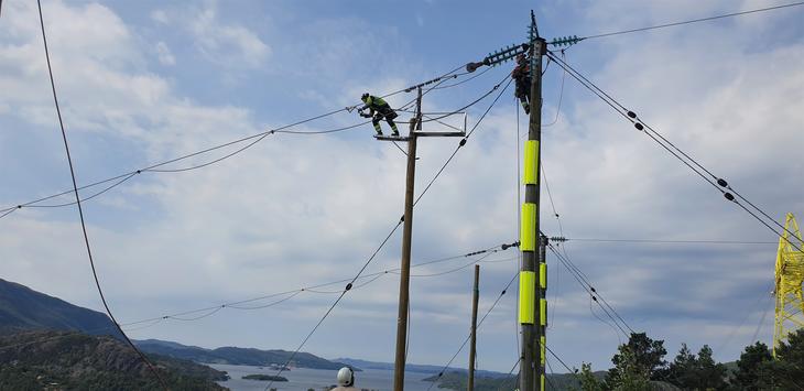 Montør jobber i toppen av fjordspennet med bytte linetråd på 50 kV over Årdalsfjorden