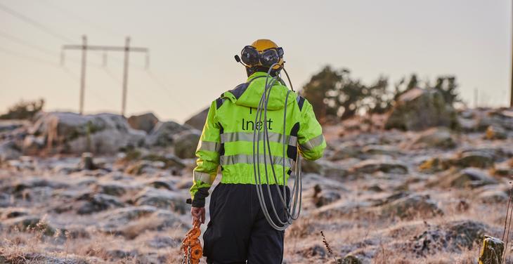 Montør i gul bekledning med ustyr over skulderen på vei ut i terrenget for en jobb på kraftlinjen en kald vintermorgen.