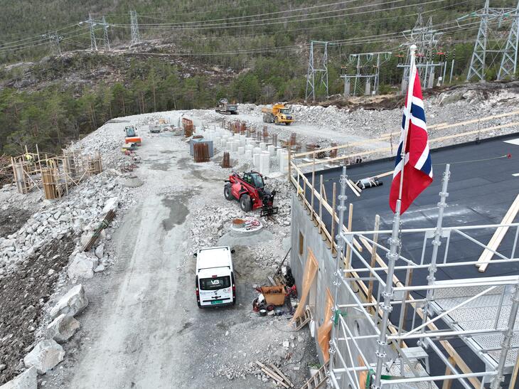 Bilde av kontrollhus med norsk flagg i toppen framme til høyre i bilde med fundament for utendørsanlegg bak. 